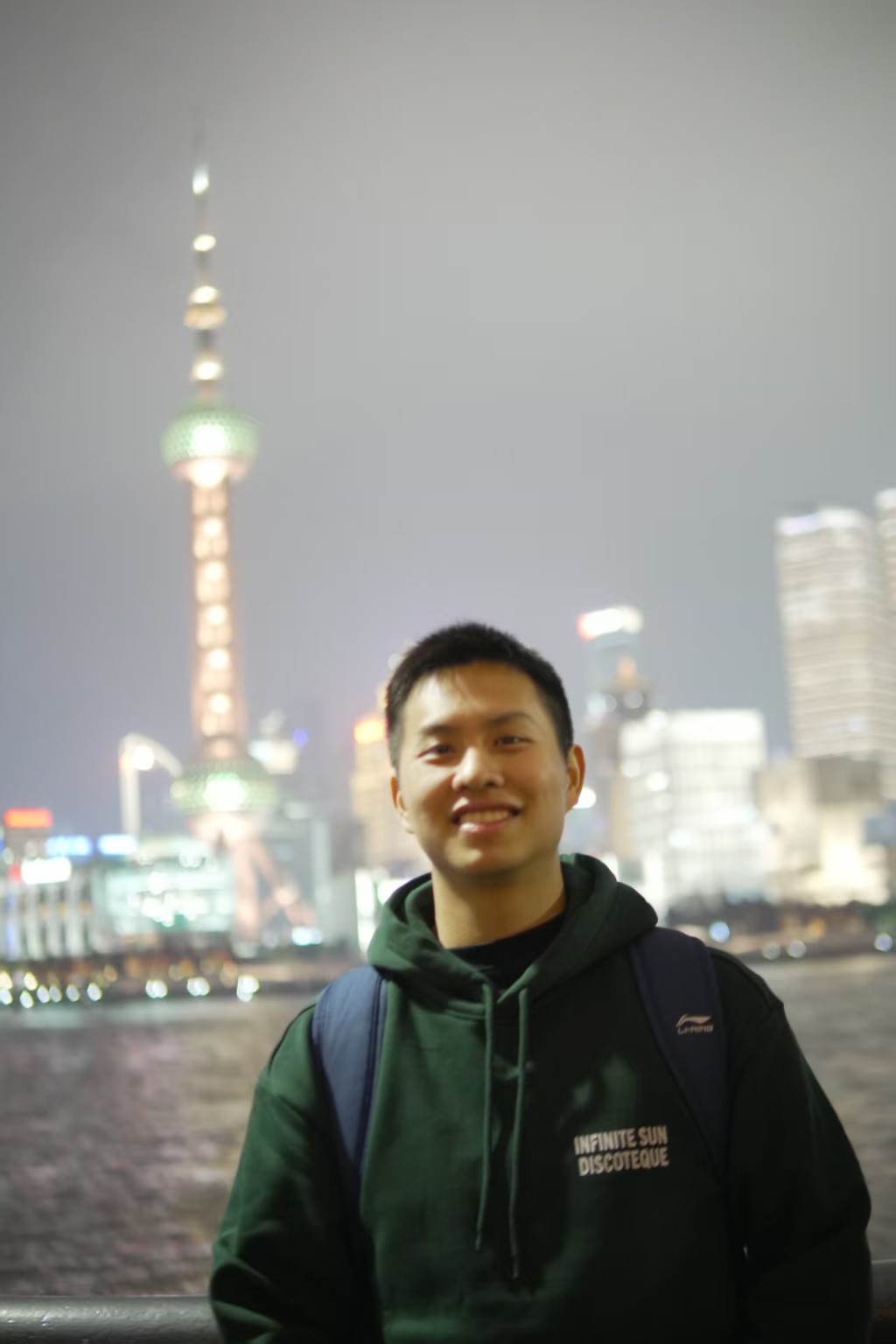 Martin smiling at night on the Shanghai waterfront, the Oriental Pearl Tower illuminated behind him.